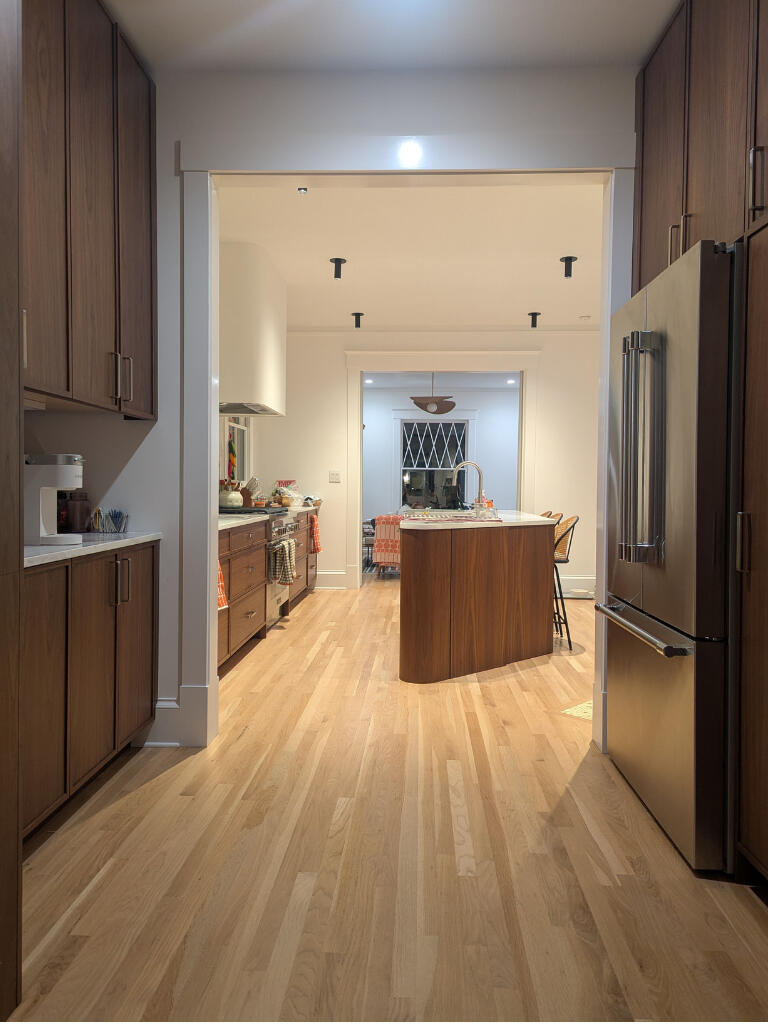 A spacious kitchen and dining area with warm wood cabinetry, soft lighting, and a clean, inviting layout. The room transitions seamlessly from cooking to gathering, reflecting comfort and care.